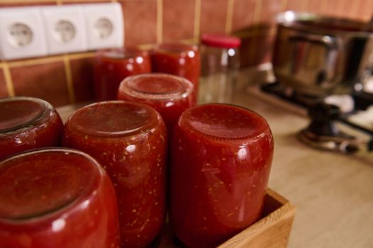 Still life with sterilized jars of freshly canned tomato sauce, passata from organic homegrown juicy tomatoes Rio Grande, or juice upside down on a wooden crate. Canning vegetables for winter.