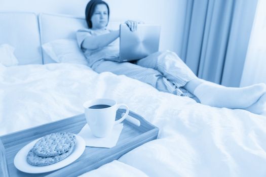 Woman in bed with laptop and a breakfast