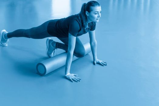 Attractive female doing foam roller exercise and posing in modern bright fitness center