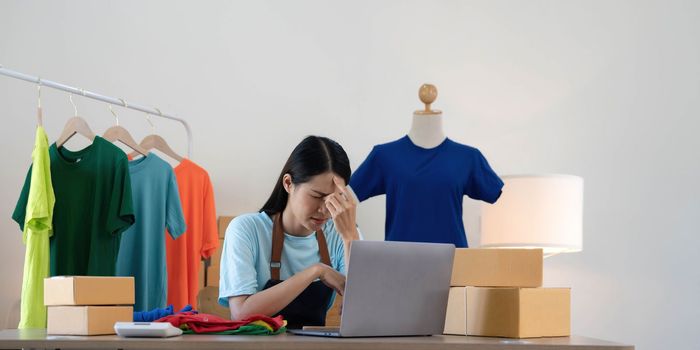 Woman seller SME retail store owner work hard worry stress in bad news on laptop at home office desk. Asian people crisis tailor job issue feel tired tough and upset in cash money loss or loan debt..