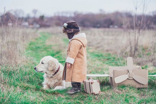 Charming sad baby in aviator's clothes says goodbye to the dog before the flight