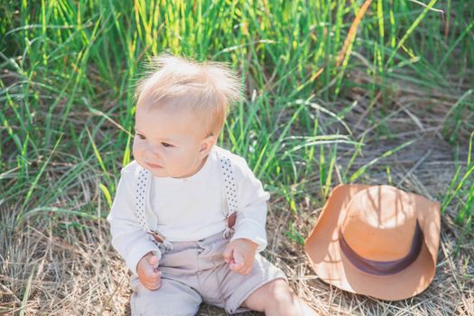 charming baby in a hat and suspenders in the field.