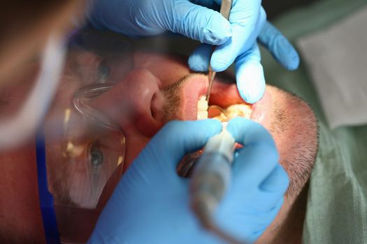 Man treats teeth in dental clinic closeup. Modern dentistry and healthcare concept.