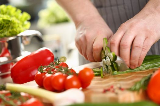 Cook cuts cucumbers on board with vegetables in kitchen. Preparing fresh tasty healthy salad