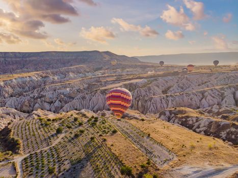 Colorful hot air balloons flying over at fairy chimneys valley in Nevsehir, Goreme, Cappadocia Turkey. Spectacular panoramic drone view of the underground city and ballooning tourism. High quality.