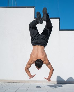 Man doing a handstand outdoors against a white wall