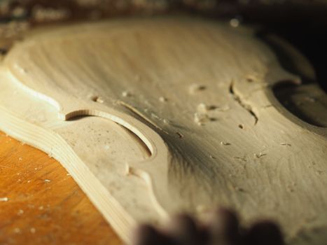 luthier working on raw wood violin plate with finger plane on the bench