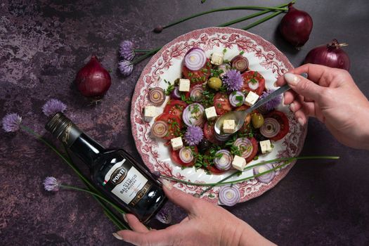 As,Belgium, May 10, 2022: tomato salad with purple onion rings dressed with Ponti balsamic dressing and olive oil with feta cheese and olives on a dark purple background, step by step recipe,flat lay