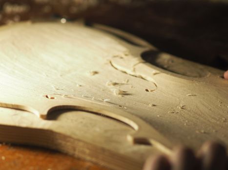 luthier working on raw wood violin plate with finger plane on the bench