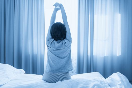 Woman stretching in bed after wake up, back view