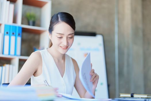 Portrait of a thoughtful Asian businesswoman looking at financial statements and making marketing plans using a computer on her desk.