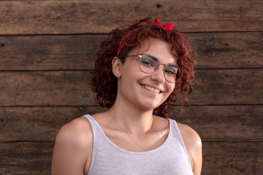 European woman with a sincere smile and short curly hair. A wall of brown-colored boards. Dressed in a gray sports T-shirt.