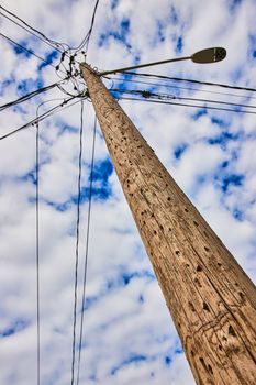 Image of Detail looking up textured wood telephone pole with spotty clouds on blue sky