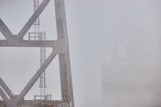 Image of Support pillars of old steel bridge with ladders fading in extreme weather foggy morning