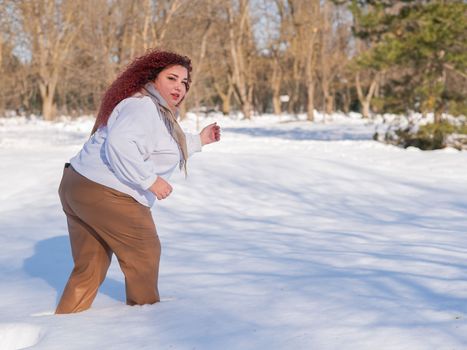 A fat red-haired woman in a white sweatshirt walks through snowdrifts