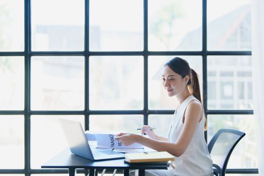 Portrait of a thoughtful Asian businesswoman looking at financial statements and making marketing plans using a computer on her desk.