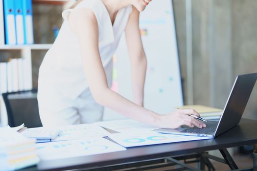 Portrait of a thoughtful Asian businesswoman looking at financial statements and making marketing plans using a computer on her desk.