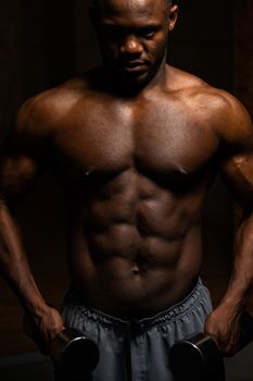 Muscular dark-skinned man doing an exercise with dumbbells