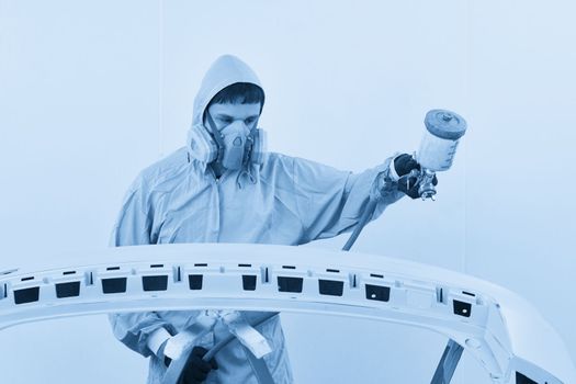 Mechanic painting bumper of a car with sprayer in painting booth