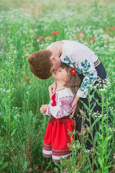 Mom in Ukrainian national dress kisses her daughter in a field with flowers