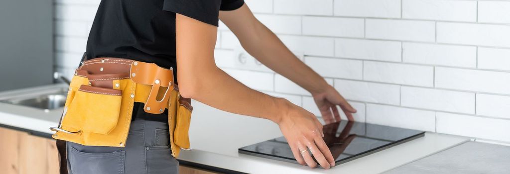 Young Repairman Installing Induction Cooker In Kitchen.