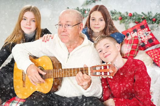 Grandfather playing guitar during christmas for grandchildren. Happy man 60s playing guitar christmas songs. Happy christmas atmosphere.