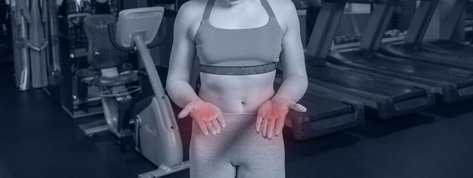 Young woman in sportswear having ache on palms after training in a gym