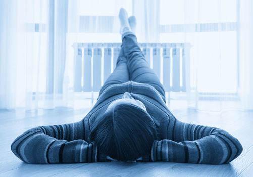 Woman laying on floor with feet raised up on radiator for warming