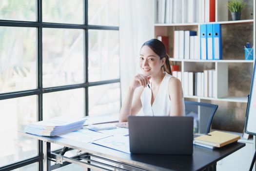 Portrait of a woman business owner showing a happy smiling face as he has successfully invested her business using computers and financial budget documents at work.