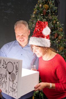 Man giving a Christmas present to his girlfriend. Great xmas surprise Beautiful young woman opening a gift box and smiling while her boyfriend hug her. Christmas wonder concept