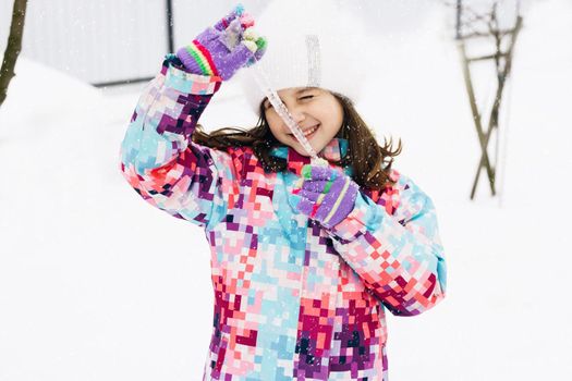 Cute child girl holding icicle. Winter portrait of little caucasian child girl wearing hat and hold big icicle. Outdoor winter activities for kids.