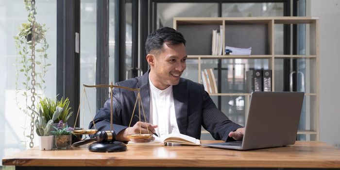 Professional Asian businessman, lawyer or financial consultant in formal suit working at his office desk, using laptop and taking notes on his book..