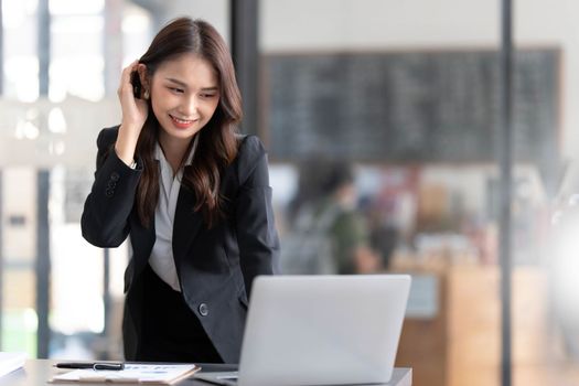 Focused young businesswoman standing at table in office, using laptop, looking at computer screen, reading or writing business email, searching information in internet, working on project..
