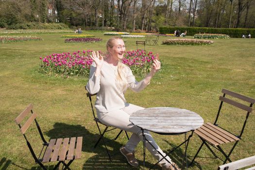 young woman in a beige jumper takes a selfie in the park with blooming tulips. High quality photo