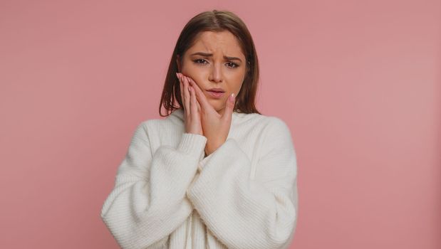 Hipster young woman touching sore cheek suffering from toothache cavities or gingivitis waiting for dentist appointment gums disease. Adult girl indoors studio shot isolated alone on pink background