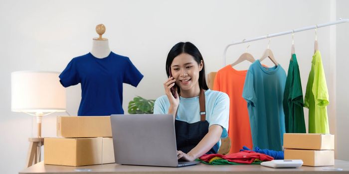 Beautiful asian woman online seller confirming orders from customer on the phone, Start small businesses SME owners female entrepreneurs use a laptop at home,pack and delivery situation concept..