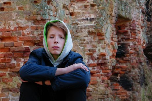 A teenager in a blue jacket with a hood poses on the background of a red old brick wall.