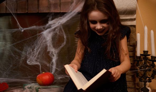 Gothic child girl, inspired witch, enchantress with a book of sorcery, sitting by a cobweb-covered fireplace mysterious candles on the candlestick, whispering spells on the Happy Halloween night
