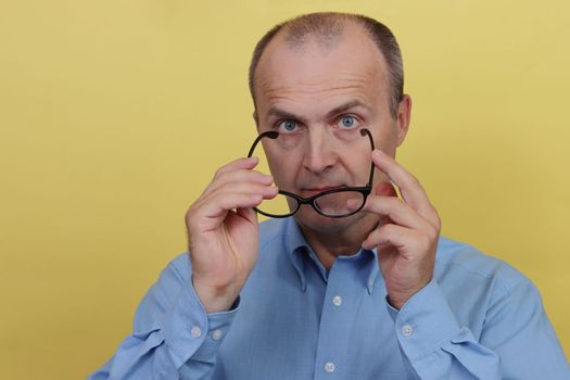 Man in blue shirt on yellow background holding transparent glasses.