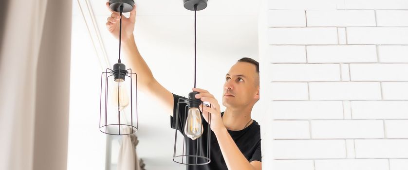 Worker repairing lamp on stretch ceiling indoors.