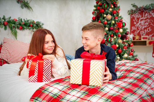 A cheerful teenagers, sister and brother, opens a Christmas gifts. Cheerful Teenagers boy and girl lies in bed with a christmas presents in they hands. Christmas themed background