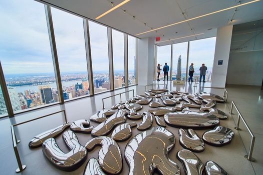 Image of Artist exhibit room metal shapes look melted with view of city outside from above