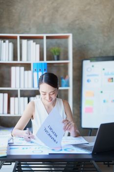 Portrait of a thoughtful Asian businesswoman looking at financial statements and making marketing plans using a computer on her desk.