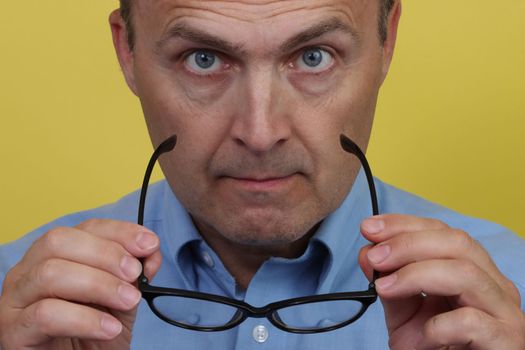 Man in blue shirt on yellow background holding transparent glasses.