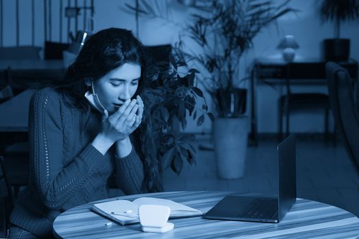 sick young woman with pills and thermometer on a table working on a laptop from home on quarantine isolation. Online work, stay home concept