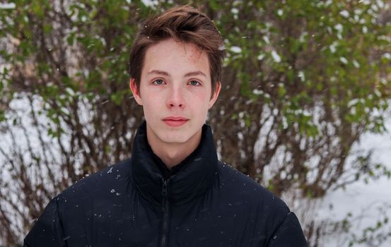 Portrait of a cute positive boy 15-17 years old in a black jacket in winter.