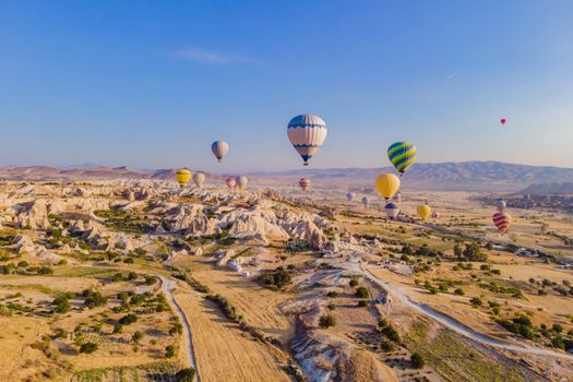 Colorful hot air balloons flying over at fairy chimneys valley in Nevsehir, Goreme, Cappadocia Turkey. Spectacular panoramic drone view of the underground city and ballooning tourism. High quality.