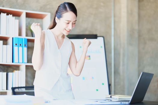 Portrait of a woman business owner showing a happy smiling face as he has successfully invested her business using computers and financial budget documents at work.