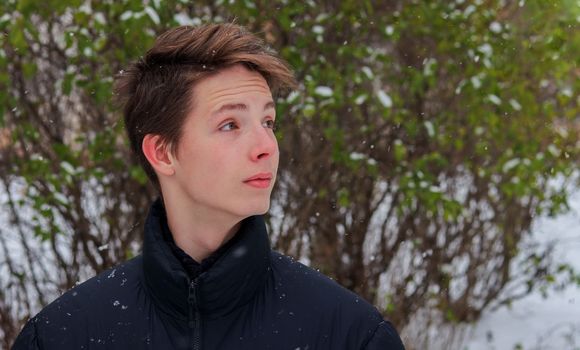 Portrait of a cute positive boy 15-17 years old in a black jacket in winter. Portrait of a boy in profile.