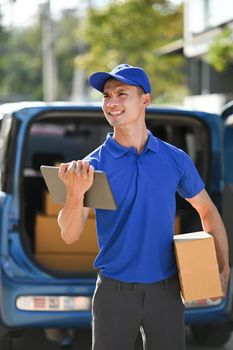 Portrait of delivery man carrying cardboard parcel and using digital tablet. Delivery service, post and shipping concept.